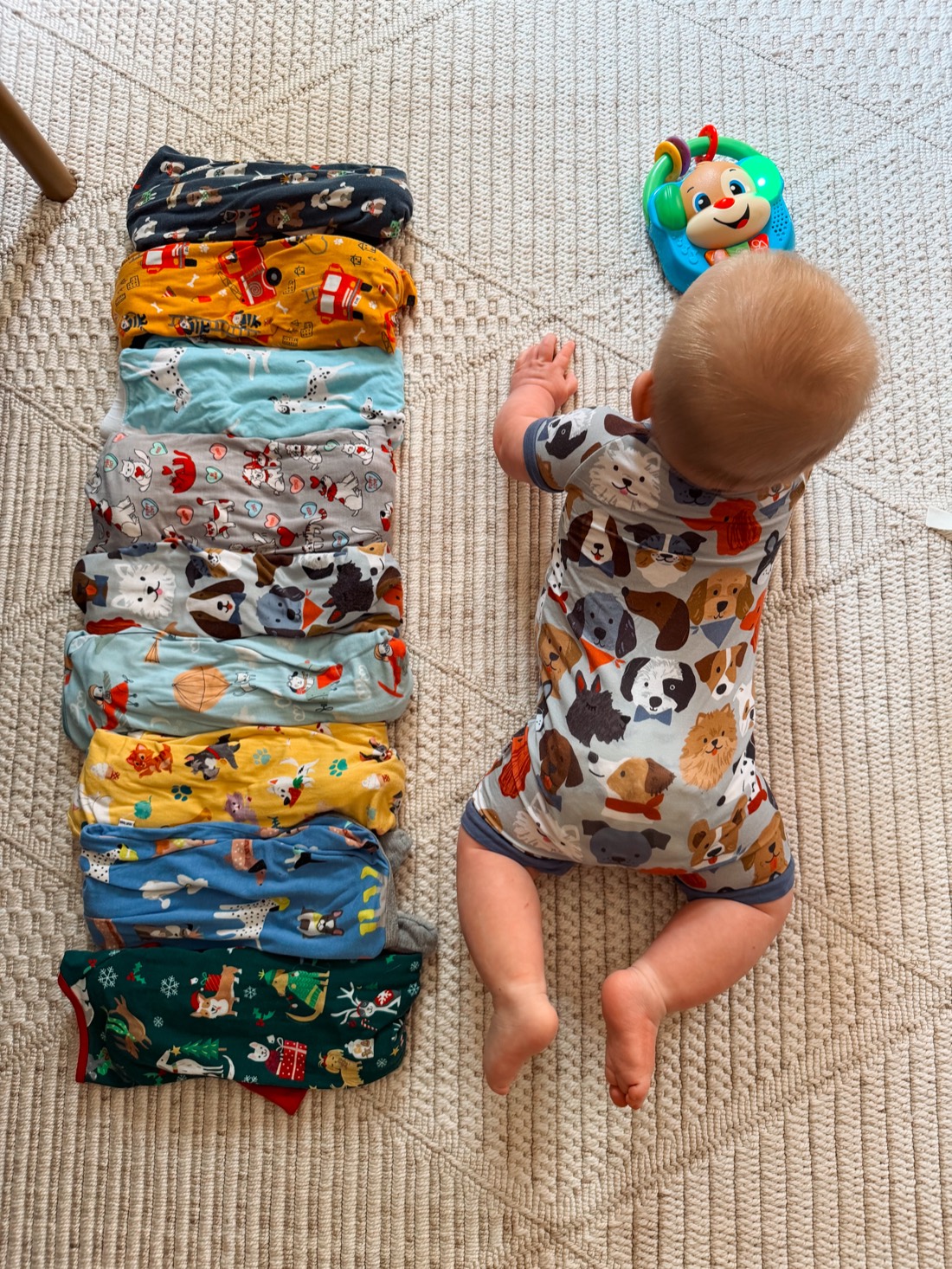 A baby beside a neatly stacked row of folded patterned pajamas
